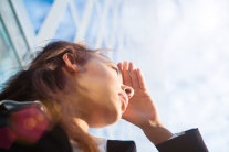 Frau blickt in die Ferne und schirmt mit der Hand die Sonne ab 