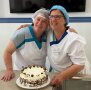 zwei Frauen in SChürzen umarmt vor einer verzierten Torte