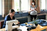 Frau sitzt neben Nähmaschine über ausgeschnittenen Jeansstücken.