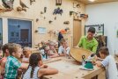 In der Holzwerkstatt betrachten Kinder mit Förster um Tisch eine Baumscheibe