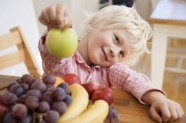 Blonder Junge hinter Obstschale mit Apfel in der Hand 