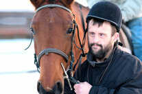 Mann mit Reiterhelm führt Pferd am Zügel.